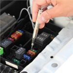 Hand using a circuit tester to check a fuse inside a car's fuse box